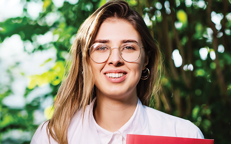 Female smiling in front of trees holding a work book