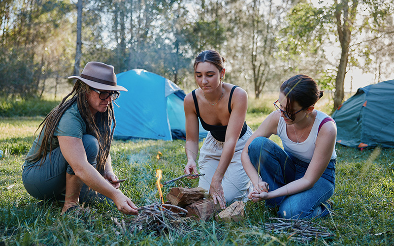 Two young girls and woman starting a fire at a campsite