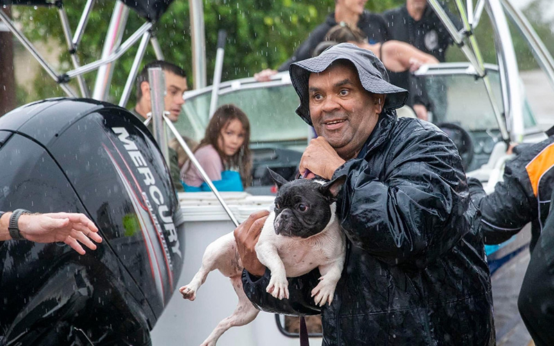 Man with dog in front of a boat rescuing people from flood