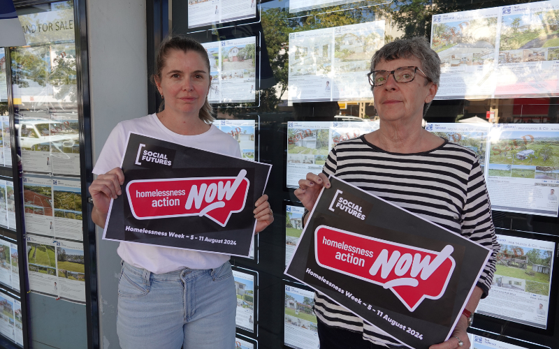 Connecting Home program workers standing in front of real estate office with homelessness week signs