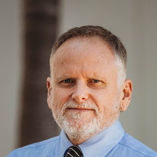 Photo of Chris Leach wearing a blue collared shirt and tie