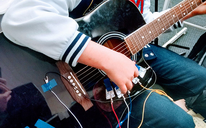 A young person plays a guitar with wires on it