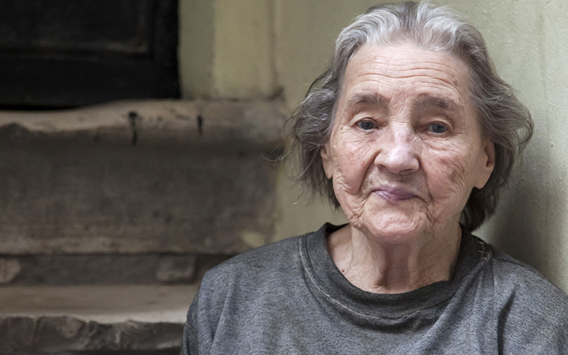 An older woman with wrinkles and grey hair wears an old grey t-shirt