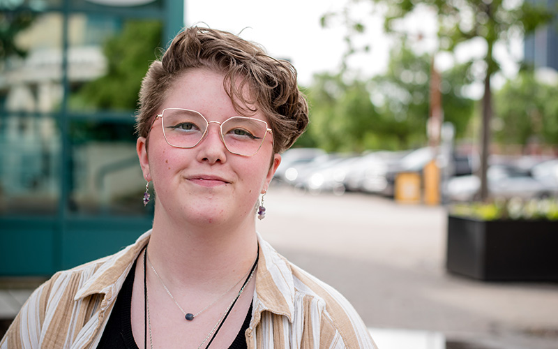 A young woman in her early 20's with short hair and glasses smiles