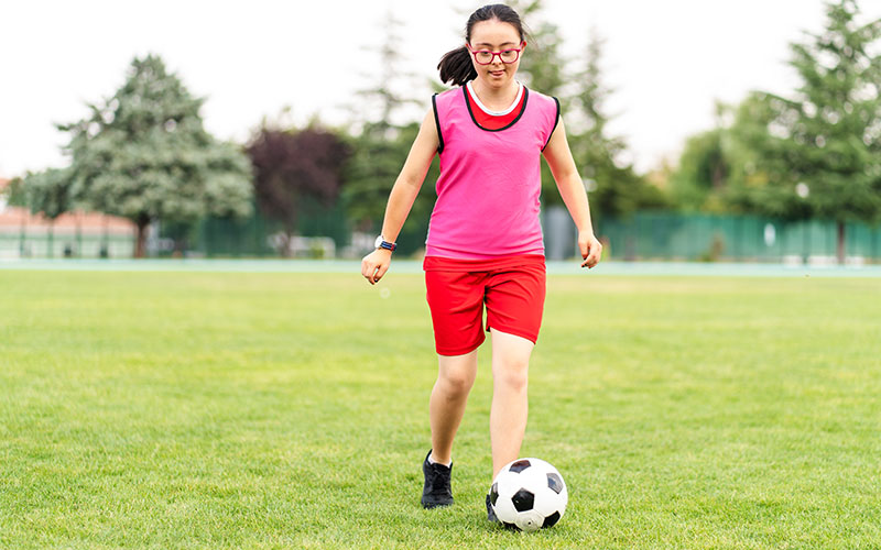 A young girl living with disability kicks a soccer ball in the park